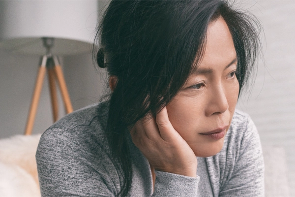 Adrenal-Fatigue-Doctor A middle-aged asian woman sitting on her couch, resting her head on her hand, suffering from adrenal fatigue. Get treatment for adrenal fatigue syndrome from Dr. Donna Diamond in Louisville/Boulder.
