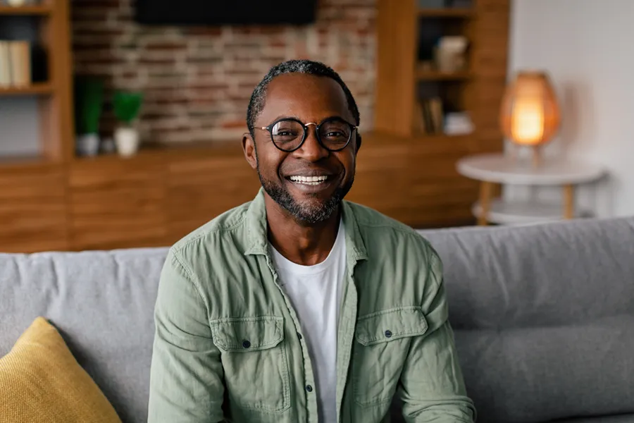 Andropause-Doctor A middle aged black man in a green button up shirt sits on his couch smiling, happy with his treatment for andropause and low testosterone from Dr. Donna Diamond in Louisville/Boulder.
