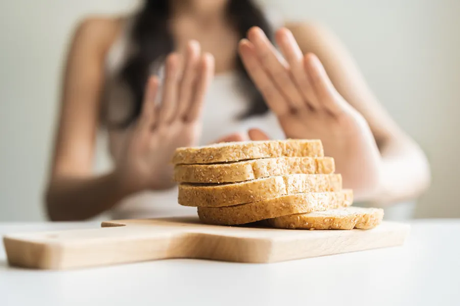Celiac-Disease-Clinic Close up of a stack of bread slices on a cutting board with a woman's hands behind them, refusing to eat. Get treatment for Celiac Disease from Dr. Donna Diamond in Louisville/Boulder.