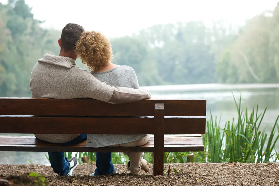 Functional-Medicine-Doctor A couple wearing sweaters seen from behind sitting on a bench and looking out at a relaxing lake and forest, representing functional medicine treatment from Dr. Donna Diamond in Louisville/Boulder.