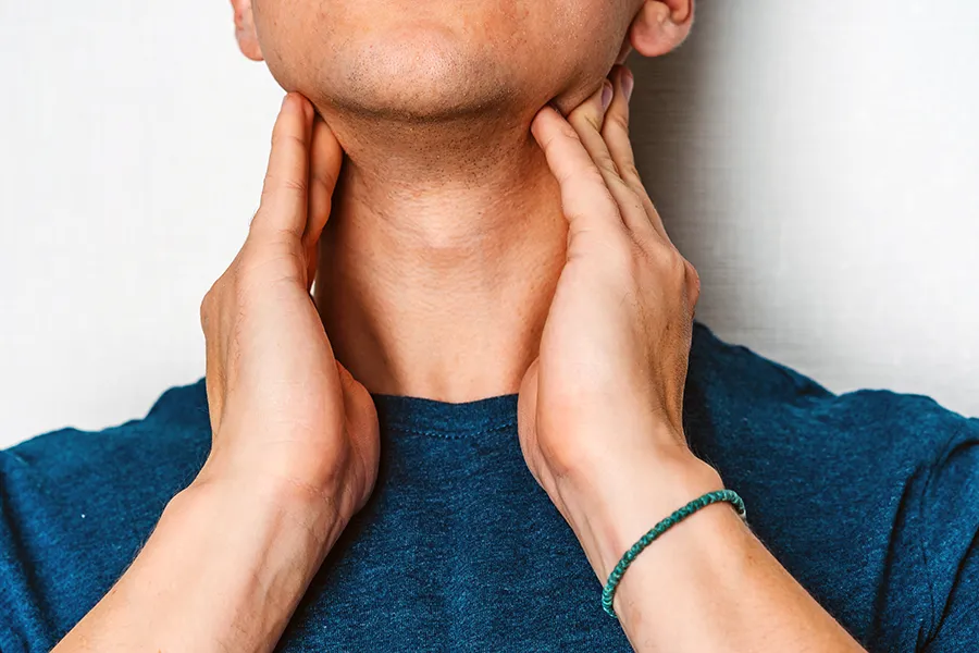 Hypothyroidism-Clinic A man in a dark teal shirt rubs the lymph nodes on his neck. Get hypothyroidism treatment from Dr. Donna Diamond in Louisville/Boulder.