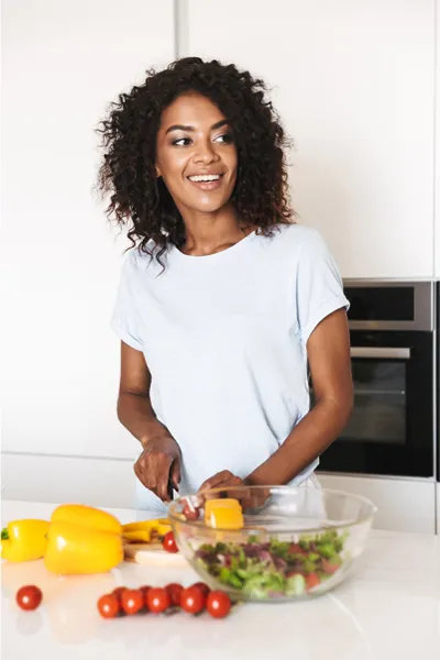 Irritable-Bowel-Syndrome-Treatment Image featuring a smiling woman chopping vegetables for a salad in a bright, white kitchen. Dr. Donna Diamond offers Irritable Bowel Syndrome Treatment and Digestive Support in Louisville/Boulder.