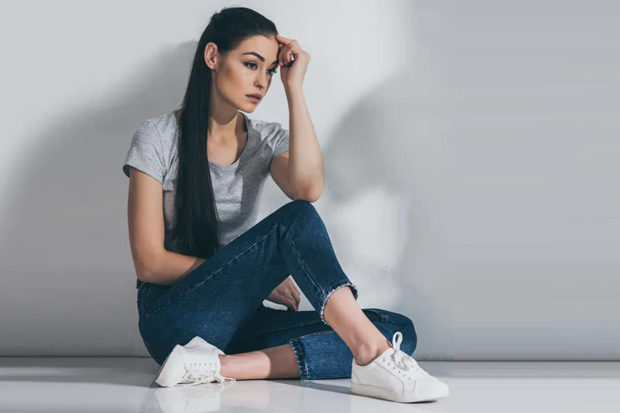 PCOS-Doctor A young brunette woman in a gray t-shirt and jeans sits against a gray wall with her head resting on her hand and a distressed expression. Get help for Polycystic Ovarian Syndrome (PCOS) from Dr. Donna Diamond in Louisville/Boulder.