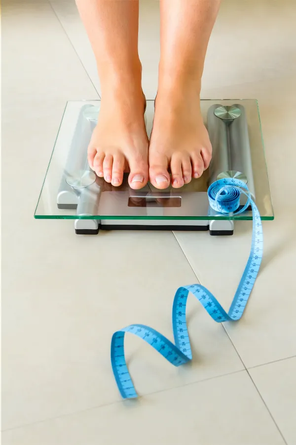 Weight-Loss-Resistance-Treatment Close-up of a woman's feet standing on a scale, with measuring tape by her toes, getting treatment for weight loss resistance from Dr. Donna Diamond in Louisville/Boulder.